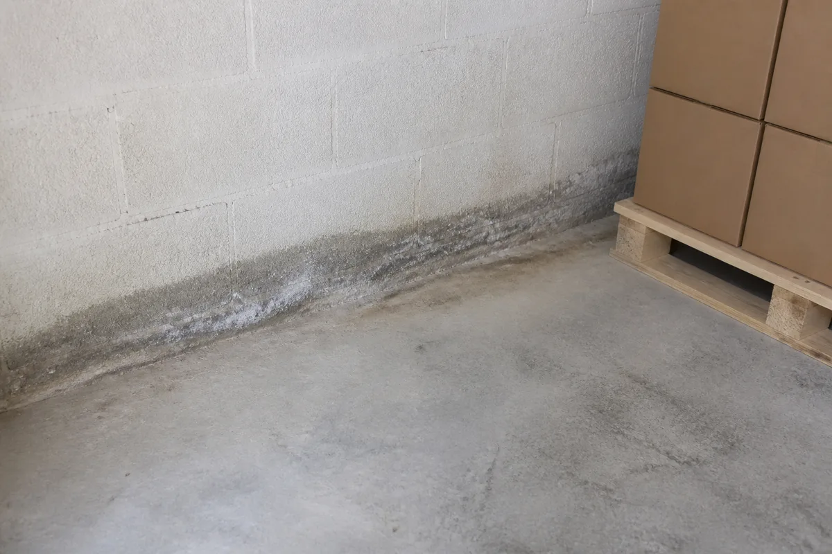 Dalle béton brute d’un garage avec traces sombres au pied du mur