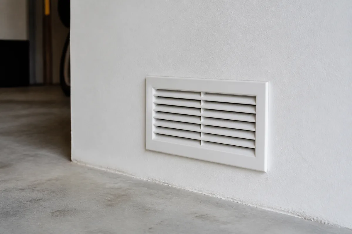 Grille d’aération basse encastrée dans un mur de garage clair